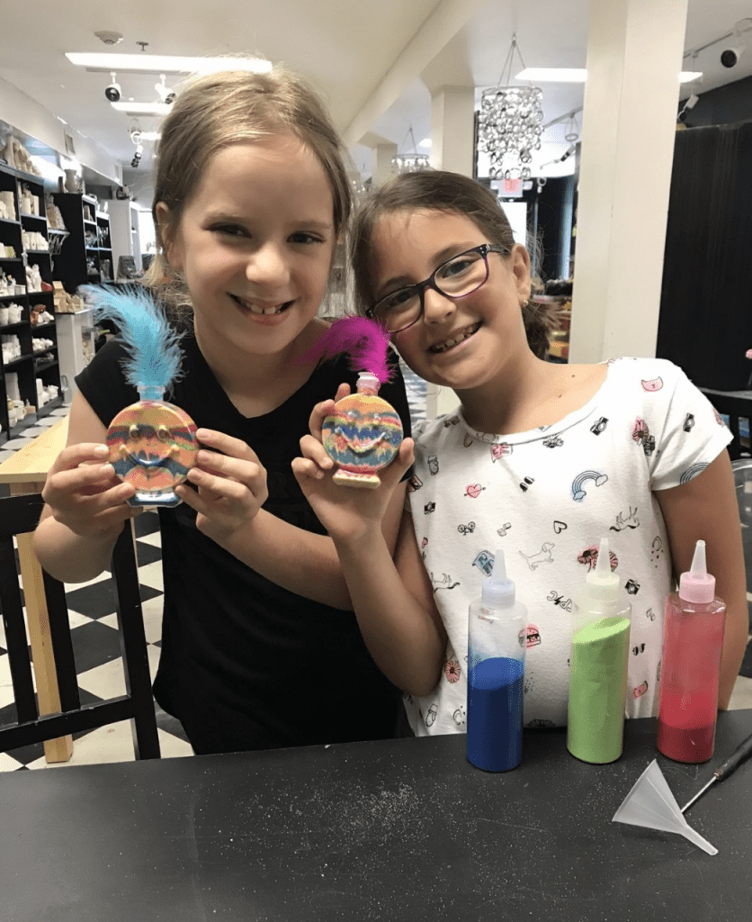 Happy faces of children proudly displaying their completed art projects at Sunshine Pottery