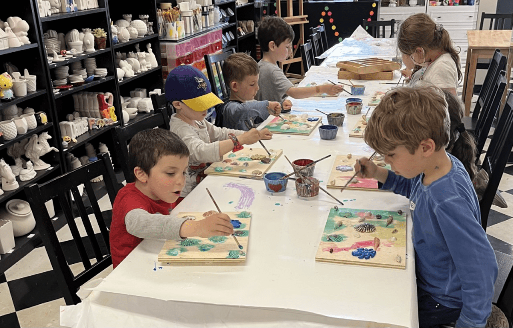 A group of kids having a blast at a glow party, creating vibrant artwork at Sunshine Pottery & Paint